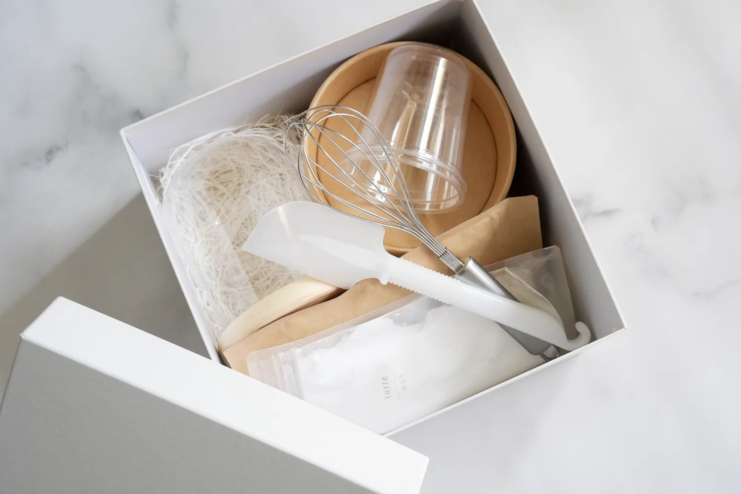 白い箱に詰められたキットの中身。泡立て器、ヘラ、透明なカップ、型取り材と石こうの袋、木製の台座が入っている