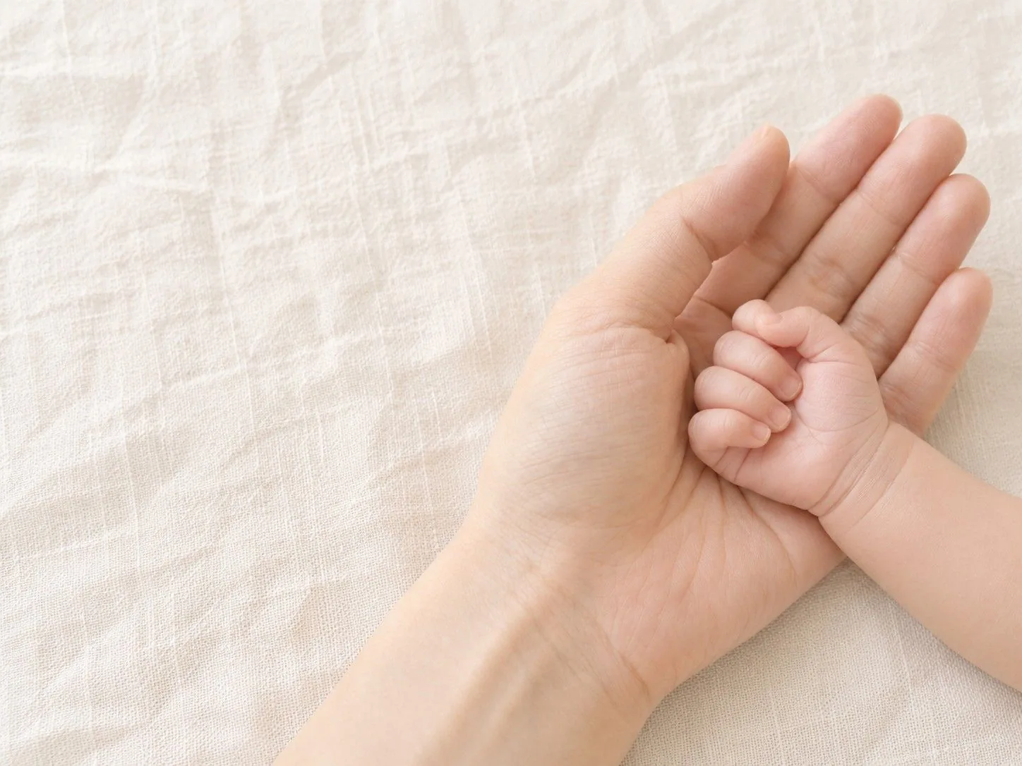 大人の手のひらに、生まれて間もない赤ちゃんの手がそっと重ねられている様子