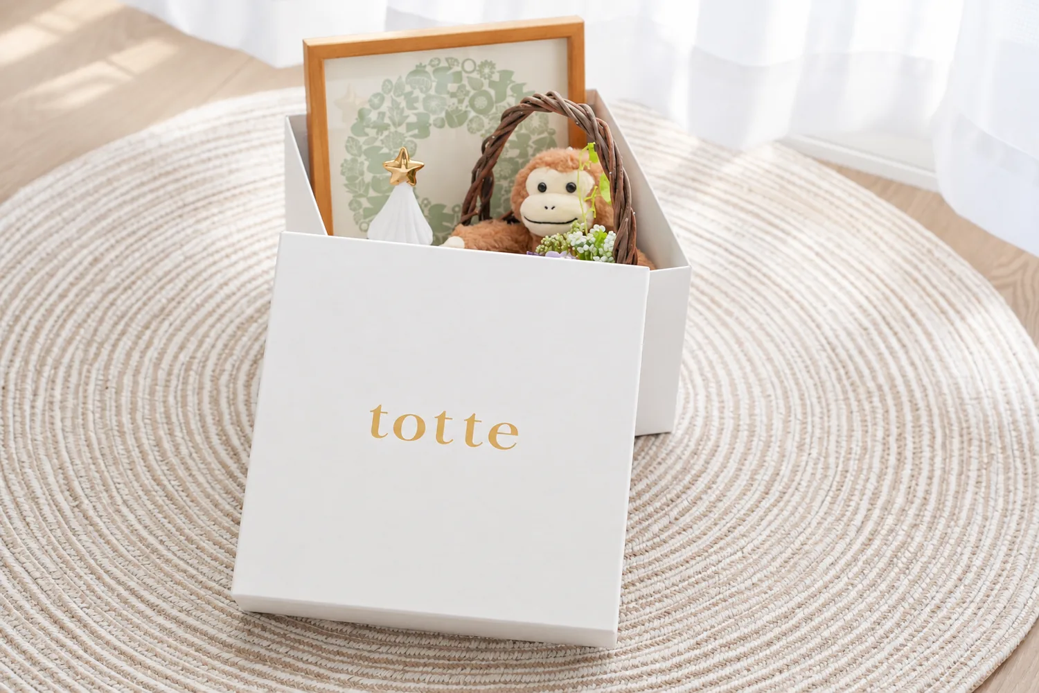 ふたを開けた白いtotteの箱に、写真立てやぬいぐるみなどの思い出の品をしまっている様子