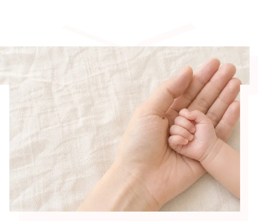 大人の手のひらに、生まれて間もない赤ちゃんの手がそっと重ねられている様子。リボン付きのギフトボックスの形に切り抜いた写真