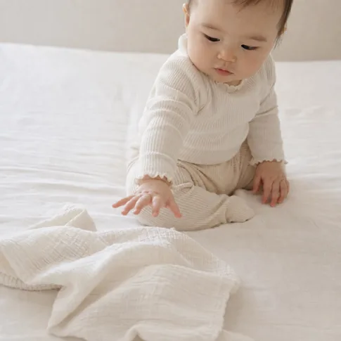 お座りした赤ちゃんがガーゼタオルに手を伸ばしている様子