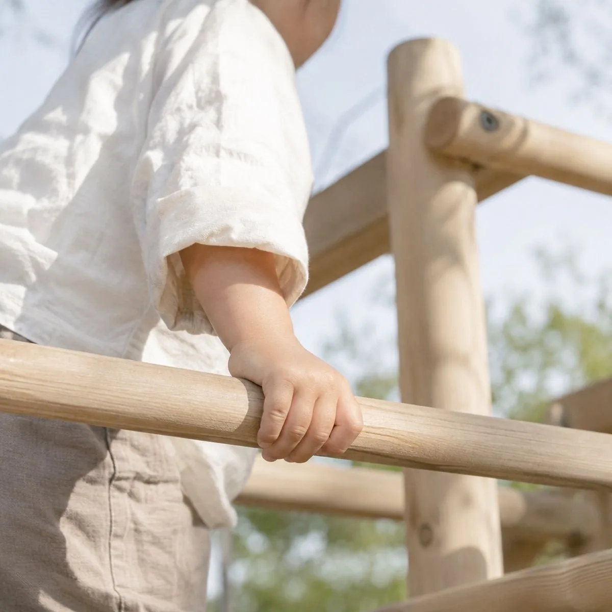 公園の木製遊具の横木を、子どもがしっかり握っている様子