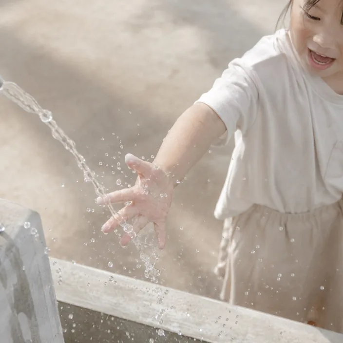 子どもが水しぶきに手を伸ばして笑っている様子