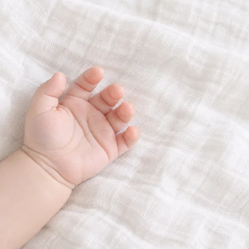 白いおくるみの上で、赤ちゃんが手のひらを開いている様子