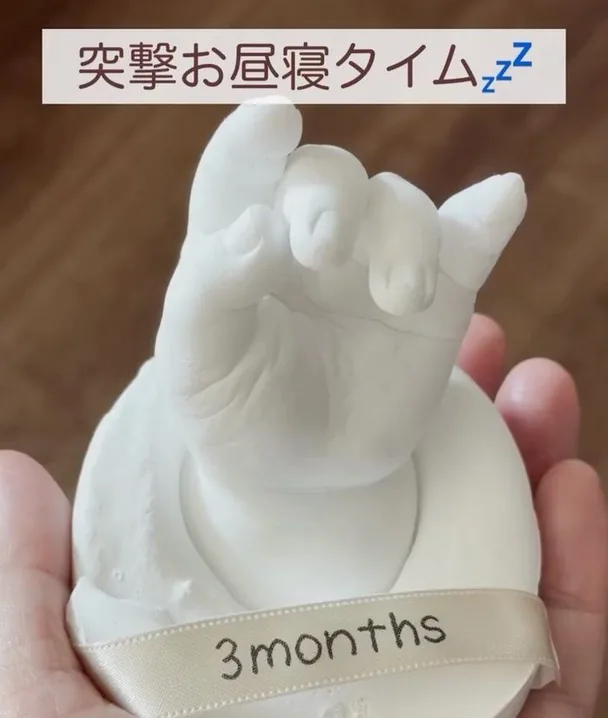 3monthsのリボンを結んだ白い立体手型を手にのせている様子。突撃お昼寝タイムというリール投稿画像