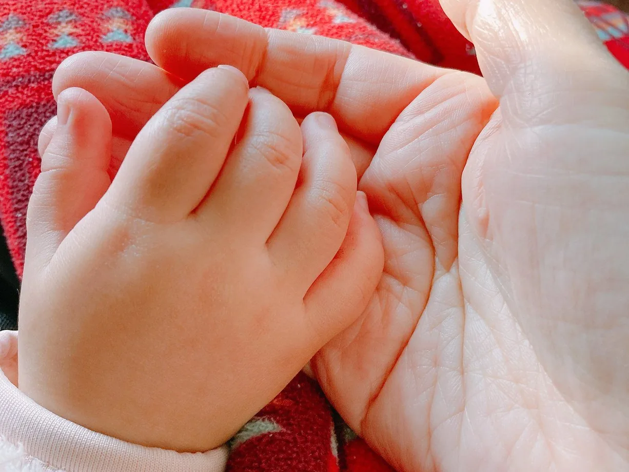 大人の手のひらに、赤ちゃんの手がそっと重ねられている様子