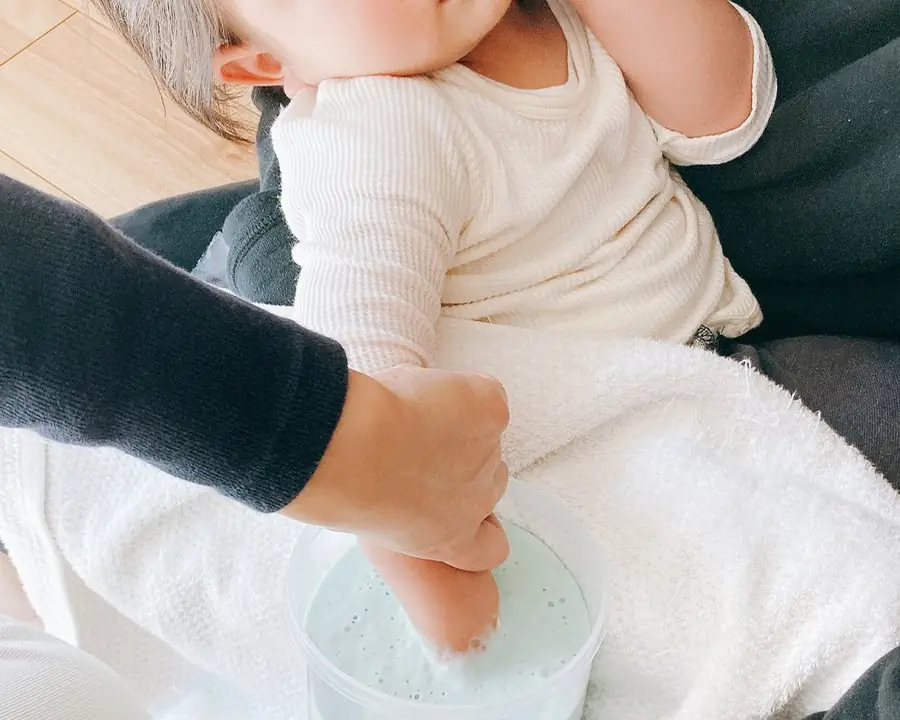 床に座って、大人2人がかりで赤ちゃんの手を型どり材の容器に入れている様子
