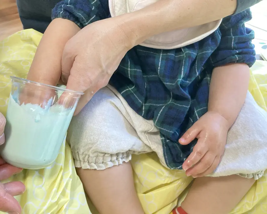 大人のひざに座った子どもの手に大人がそえて、型どり材の入った容器に入れている様子