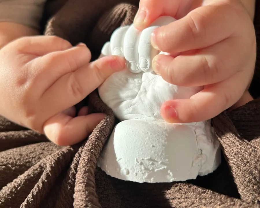 赤ちゃんの小さな手が、完成した白い立体手型にそっと触れている様子