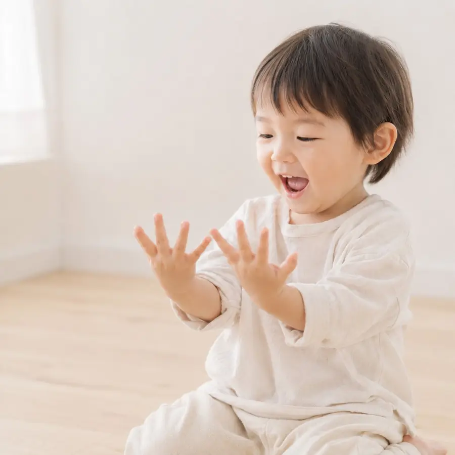 明るい部屋で、子どもが両手のひらを広げてうれしそうに見つめている様子